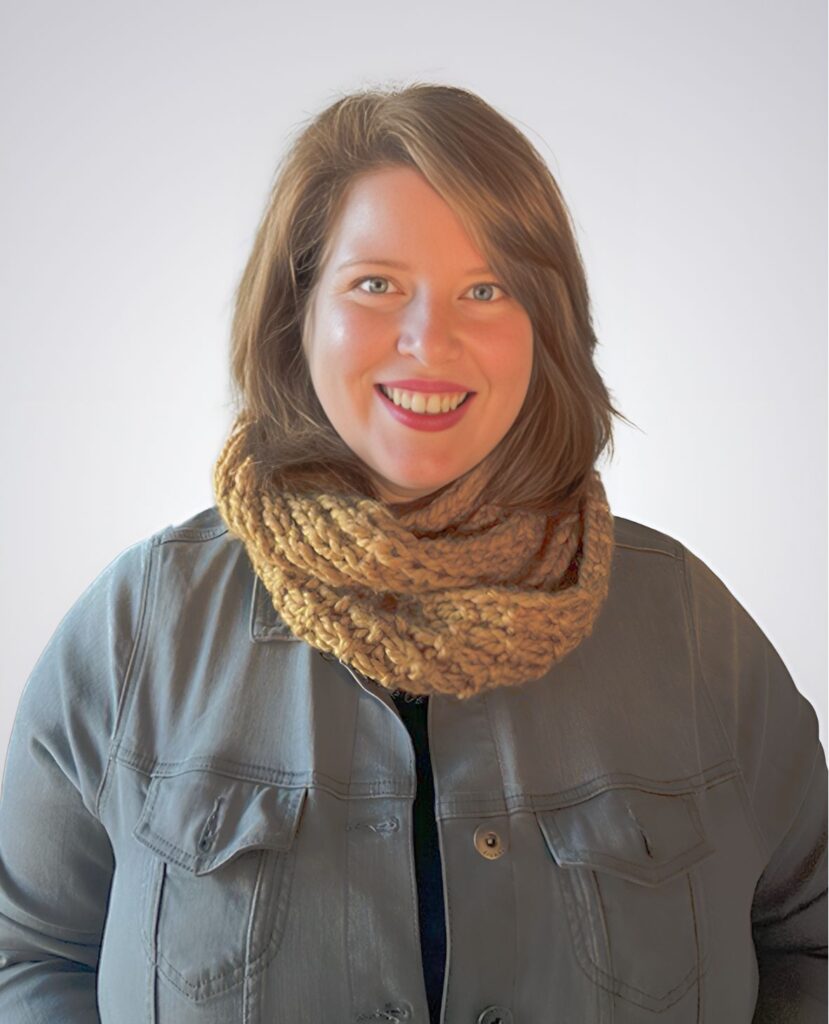 Professional headshot of a red haired woman smiling in a denim long sleeve shirt and a scarf - Dawn Voelker