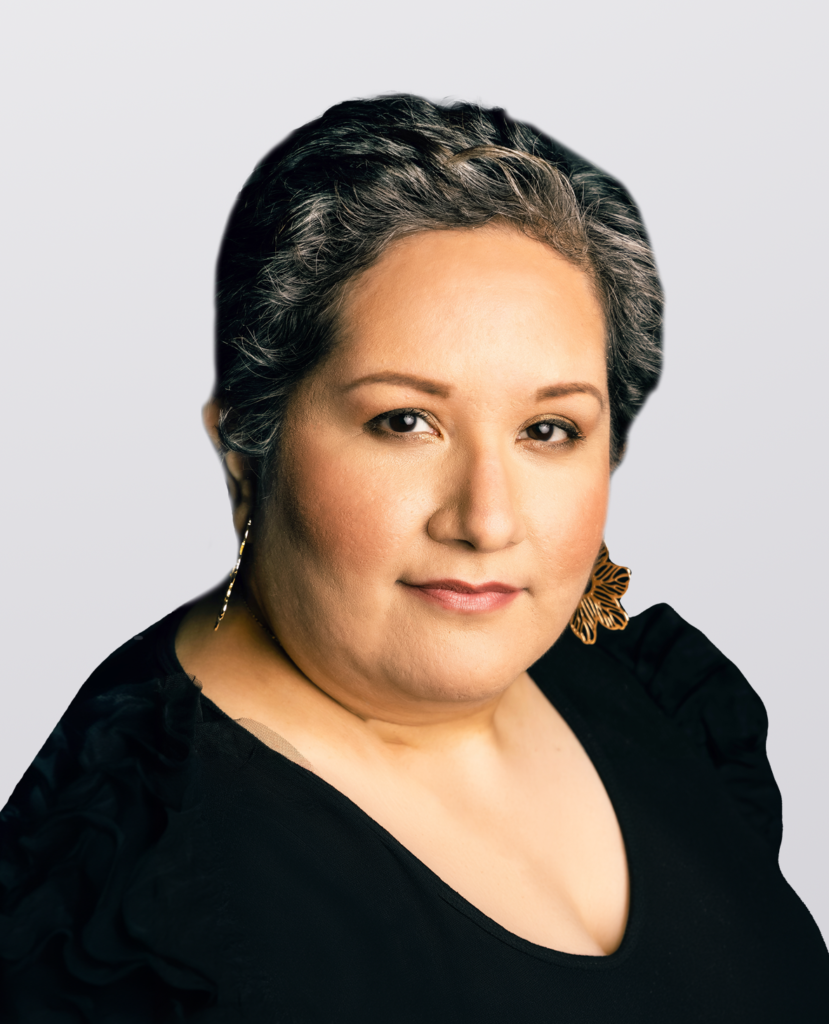 Silvia Manrique - Professional headshot of a woman smiling wearing a black dress on a light grey background