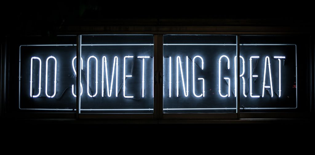 The text "do something great" capitalized made by a white neon sign on a black backgroun